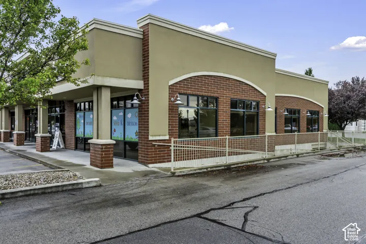 Commercial exterior featuring a brick and stucco facade, expansive storefront windows, arched masonry detailing, gooseneck light fixtures, and a paved accessible ramp