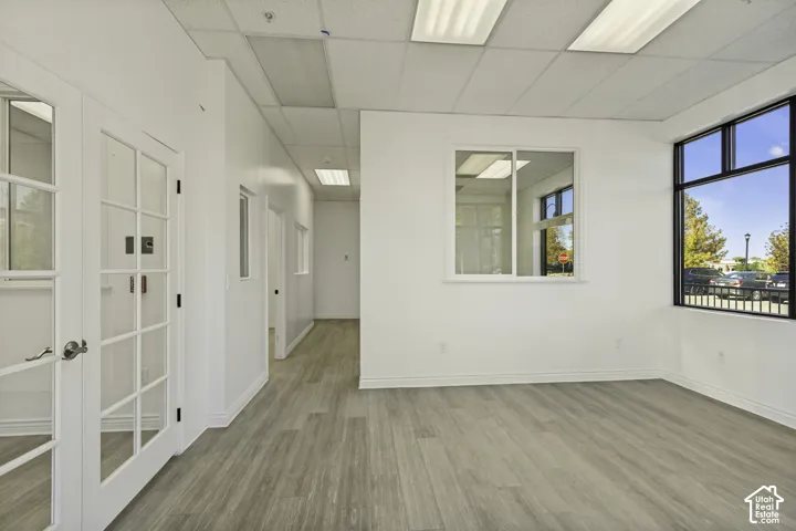 Open-concept interior featuring wood-finish flooring, drop ceiling with recessed lighting, large pane windows, and glass-paneled double doors