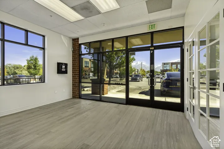 Open-concept interior featuring wood-finish flooring, extensive floor-to-ceiling glass paneling, exposed brick accent wall, and recessed drop-ceiling lighting