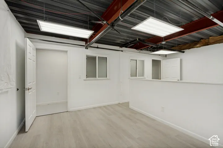 Open-concept space featuring wood-finish flooring, white walls, exposed structural steel beams, recessed ceiling panels, and dual interior doors
