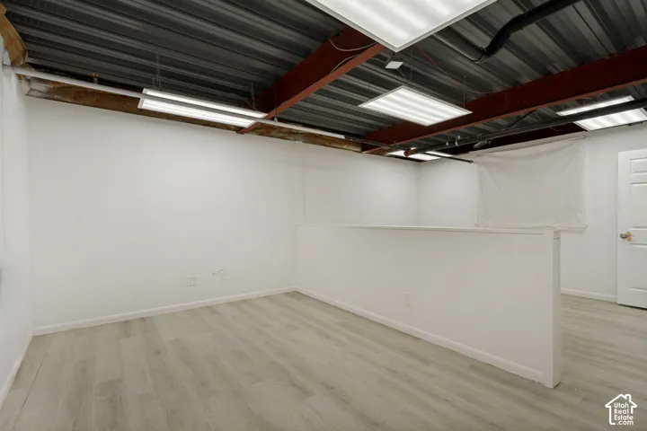 Open-concept interior featuring exposed metal ceiling joists, wood-finish flooring, recessed lighting panels, and a partial partition wall