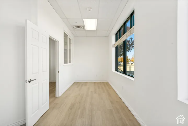 Interior space featuring light-toned wood-finish flooring, a large window with black framing, inset ceiling lighting, and a six-panel interior door