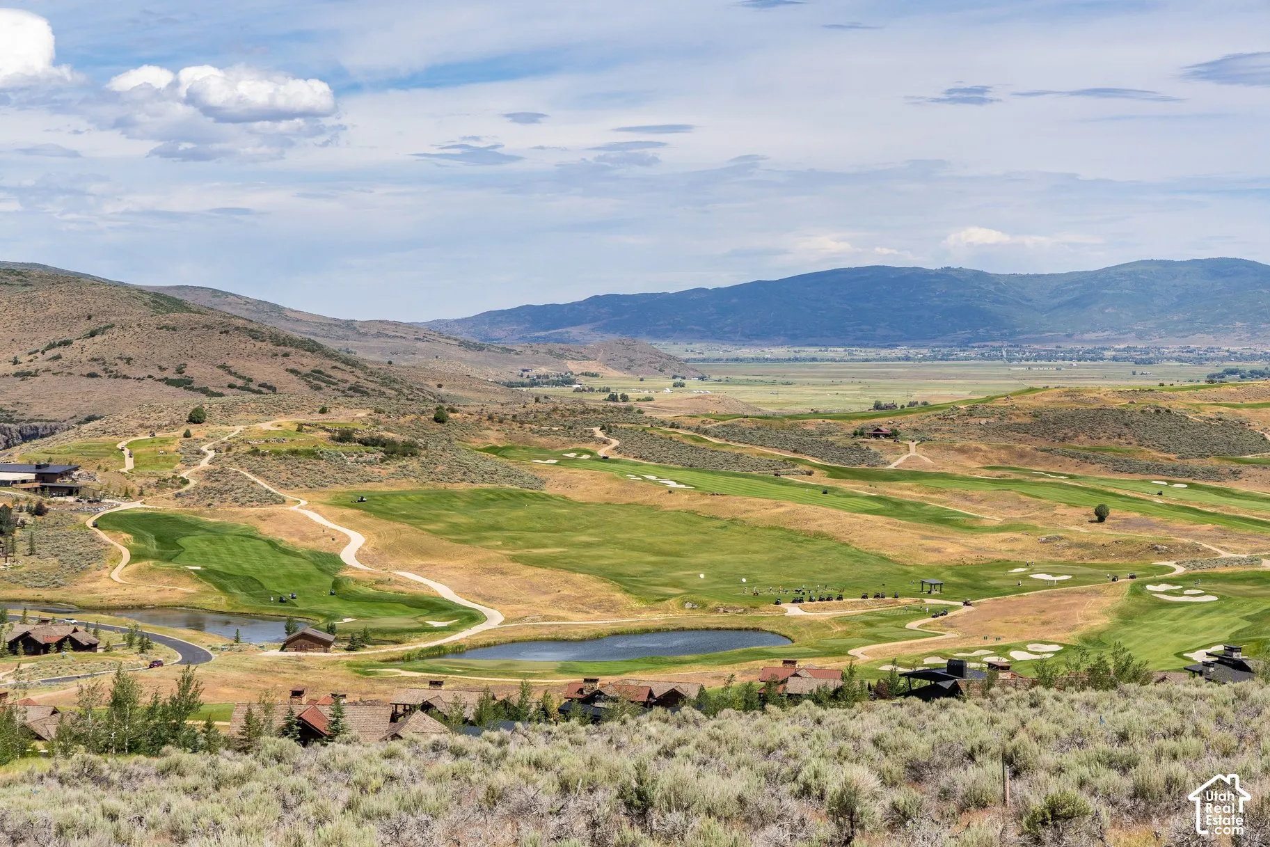 Expansive landscape featuring rolling golf course fairways, multiple water features, and a prominent mountain range backdrop
