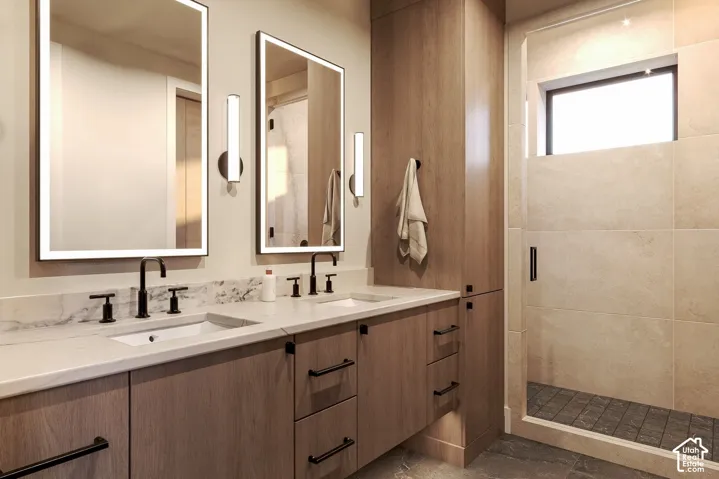 Dual-sink vanity with stone countertop, wood-finish cabinetry, backlit vanity mirrors, matte black fixtures, and a walk-in shower with stone tile surround