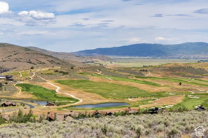 Expansive landscape featuring rolling golf course fairways, multiple water features, and a prominent mountain range backdrop