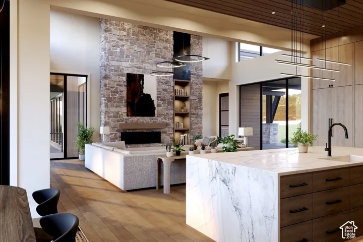 Floor-to-ceiling stone fireplace, large kitchen island with solid-surface waterfall countertop, wood-finish flooring, linear pendant lighting, and high ceilings with wood-plank detailing