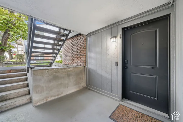 Covered exterior entryway featuring a dark-finish paneled door, vertical siding, brick accent wall, and integrated wall-mounted lighting