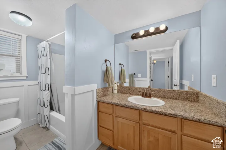 Bathroom featuring a wood vanity with a stone-finish countertop, undermount oval sink, wall-to-wall vanity mirror, wainscoting, and a tub-shower combination