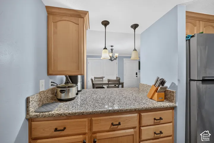 Kitchen featuring light wood-finish cabinetry, stone-patterned countertops, and dual pendant light fixtures