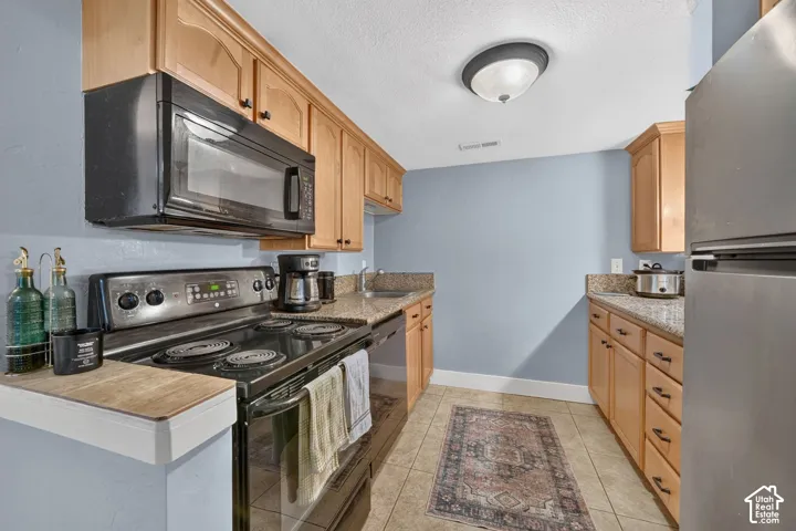 Kitchen featuring wood cabinetry, stone-finish countertops, stainless steel appliances, tile flooring, and a dome ceiling light fixture
