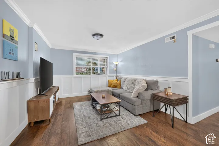 Living area featuring wood-finish flooring, crisp white board-and-batten wainscoting, crown molding, and a multi-pane window