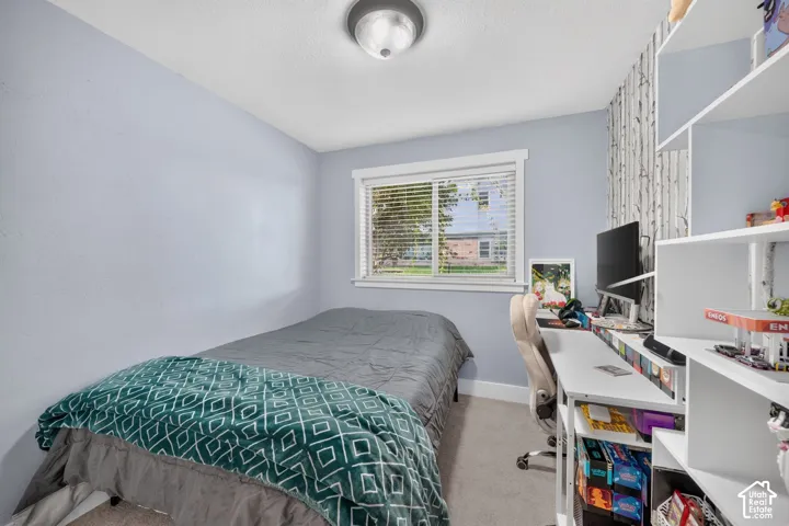 Bedroom featuring wall-to-wall carpeting, a sliding window with horizontal blinds, built-in white shelving, and a central flush-mount ceiling light fixture