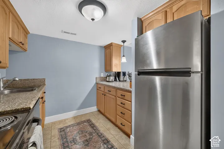 Kitchen featuring wood cabinetry, stone-finish countertops, tile flooring, and stainless steel refrigerator