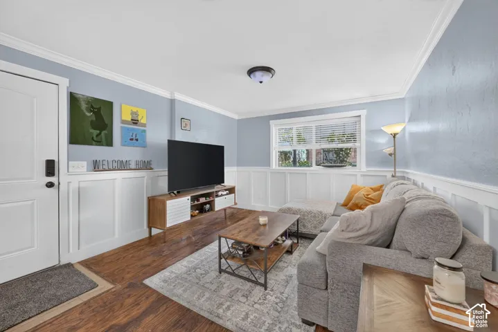 Living area featuring wood-finish flooring, crisp crown molding, and white wainscoting