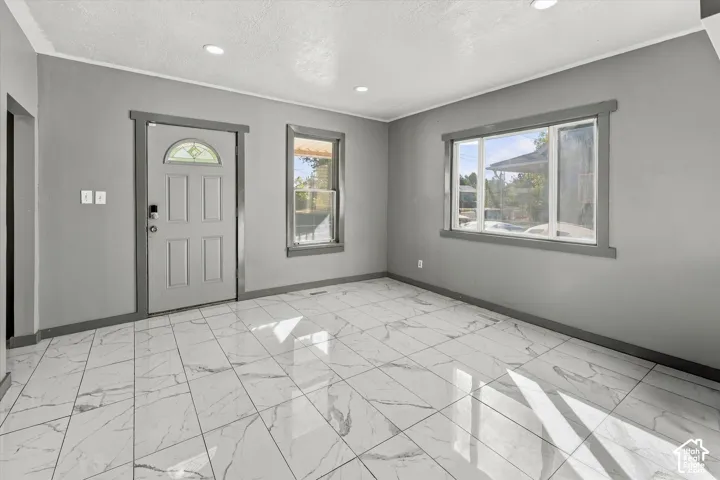 Interior space featuring large-format tile flooring with a veined pattern, recessed ceiling lighting, a multi-pane front entry door with a decorative glass insert, and wide-trim window casing