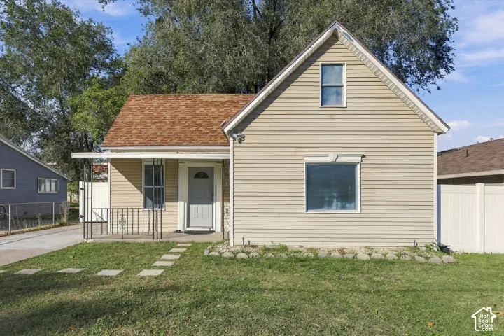 Tan siding exterior featuring an asphalt shingle roof, covered front porch with iron railing, and stone-bordered front garden bed