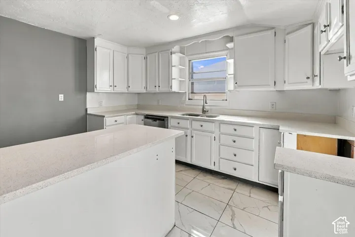 Kitchen featuring white shaker-style cabinetry, solid-surface countertops, a stainless steel undermount sink, integrated dishwasher, and marble-finish tile flooring