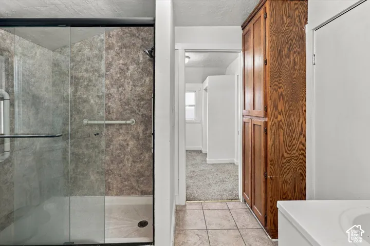 Walk-in shower featuring a sliding glass door, tiled wall surround, and mounted grab bar, paired with floor-to-ceiling wood cabinetry and ceramic tile flooring