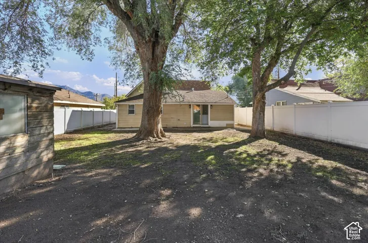 Backyard featuring mature trees, a detached wood-frame outbuilding, and perimeter white vinyl fencing