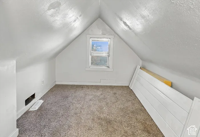 A-frame finished attic space featuring a centered single-pane window, neutral carpeting, and sloped ceiling architecture