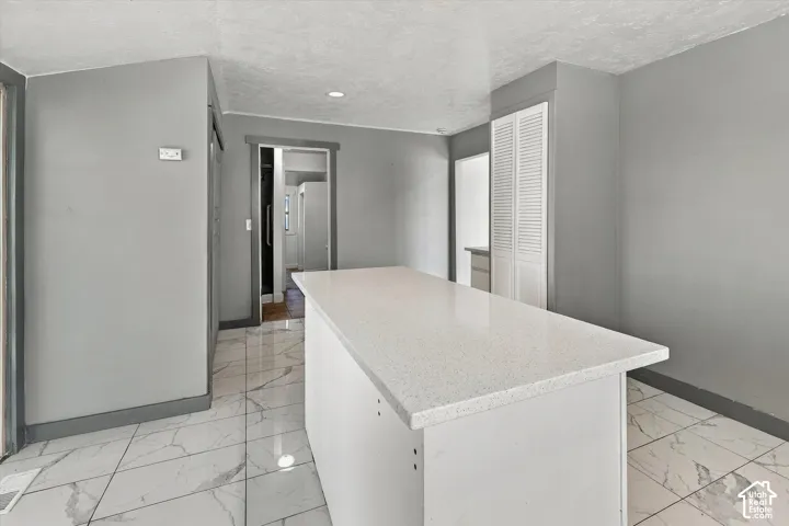 Kitchen featuring a central island with a solid-surface countertop, white louvered-door cabinetry, and large-format tile flooring with a veined pattern