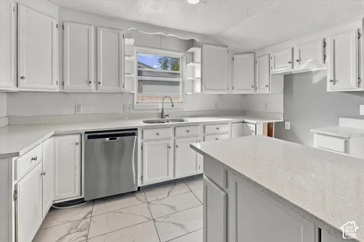 Kitchen featuring white shaker-style cabinetry, solid-surface countertops, a stainless steel dishwasher, a dual-basin sink with a gooseneck faucet, and large-format tile flooring