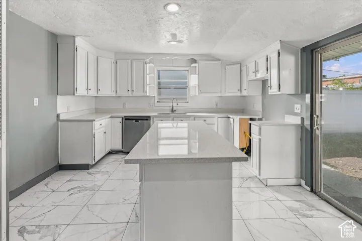 Kitchen featuring white cabinetry, quartz countertop kitchen island, stainless steel dishwasher, stone-finish tile flooring, and sliding glass door