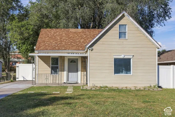 Exterior featuring vinyl siding, an asphalt shingle roof, a covered front porch with iron railings, and white privacy fencing