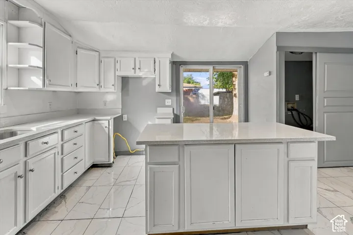 Kitchen featuring white shaker-style cabinetry, quartz countertops, a central island, tile flooring, and a sliding glass door