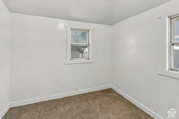 Neutral-toned wall-to-wall carpeting, smooth-finish walls, and two windows featuring white wood-casing trim