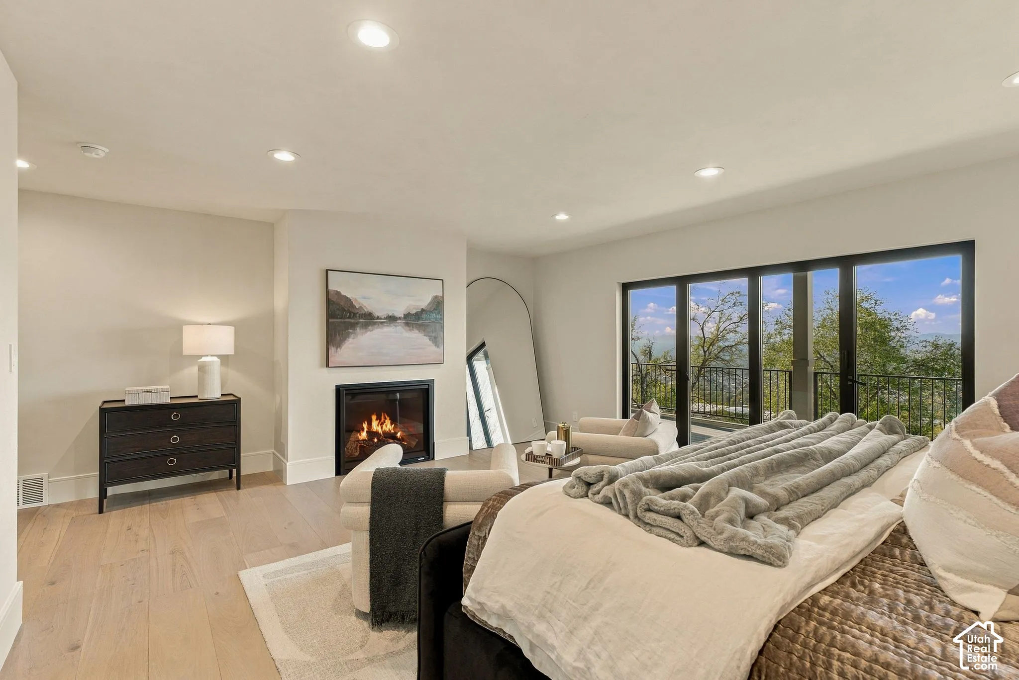 Neutral-toned room featuring recessed lighting, wood-finish flooring, a built-in fireplace with a clean-lined surround, and large-format black-frame glass doors opening to an exterior balcony