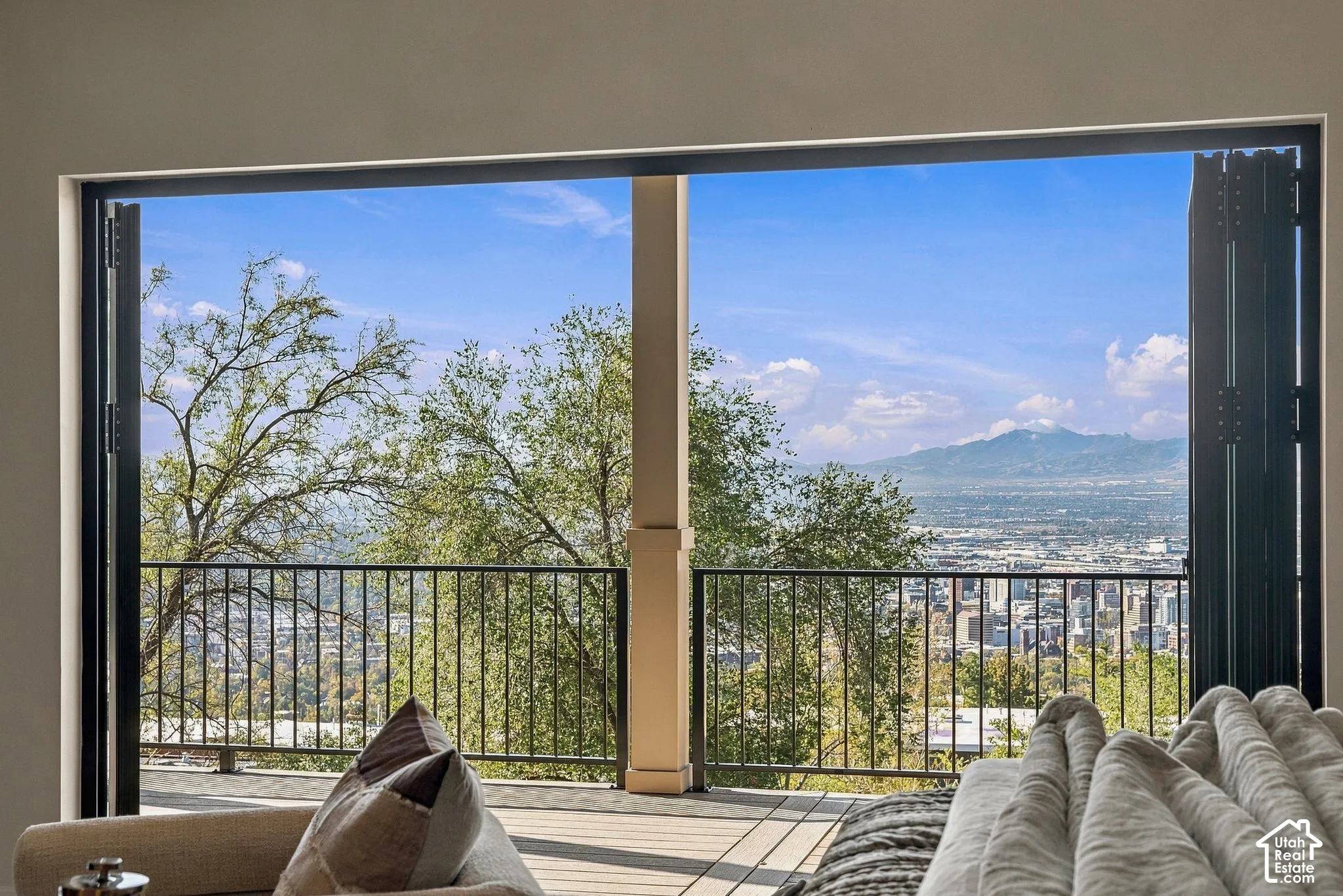 Bi-fold glass doors opening to an exterior deck with black metal railing and expansive mountain and city scenery