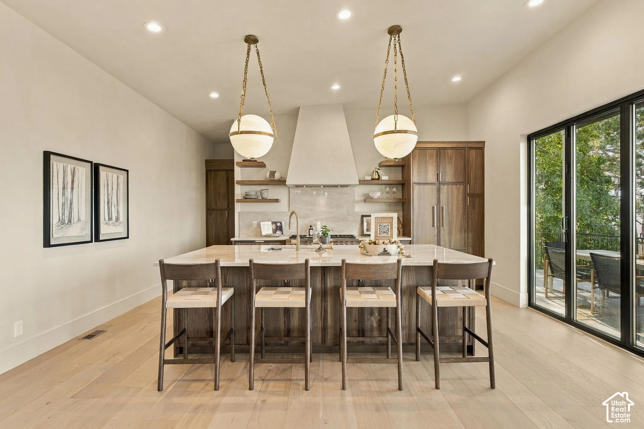 Kitchen featuring a central island with stone countertops, wood-finish cabinetry, built-in panel-front appliances, dual globe pendant lighting, and floor-to-ceiling sliding glass doors