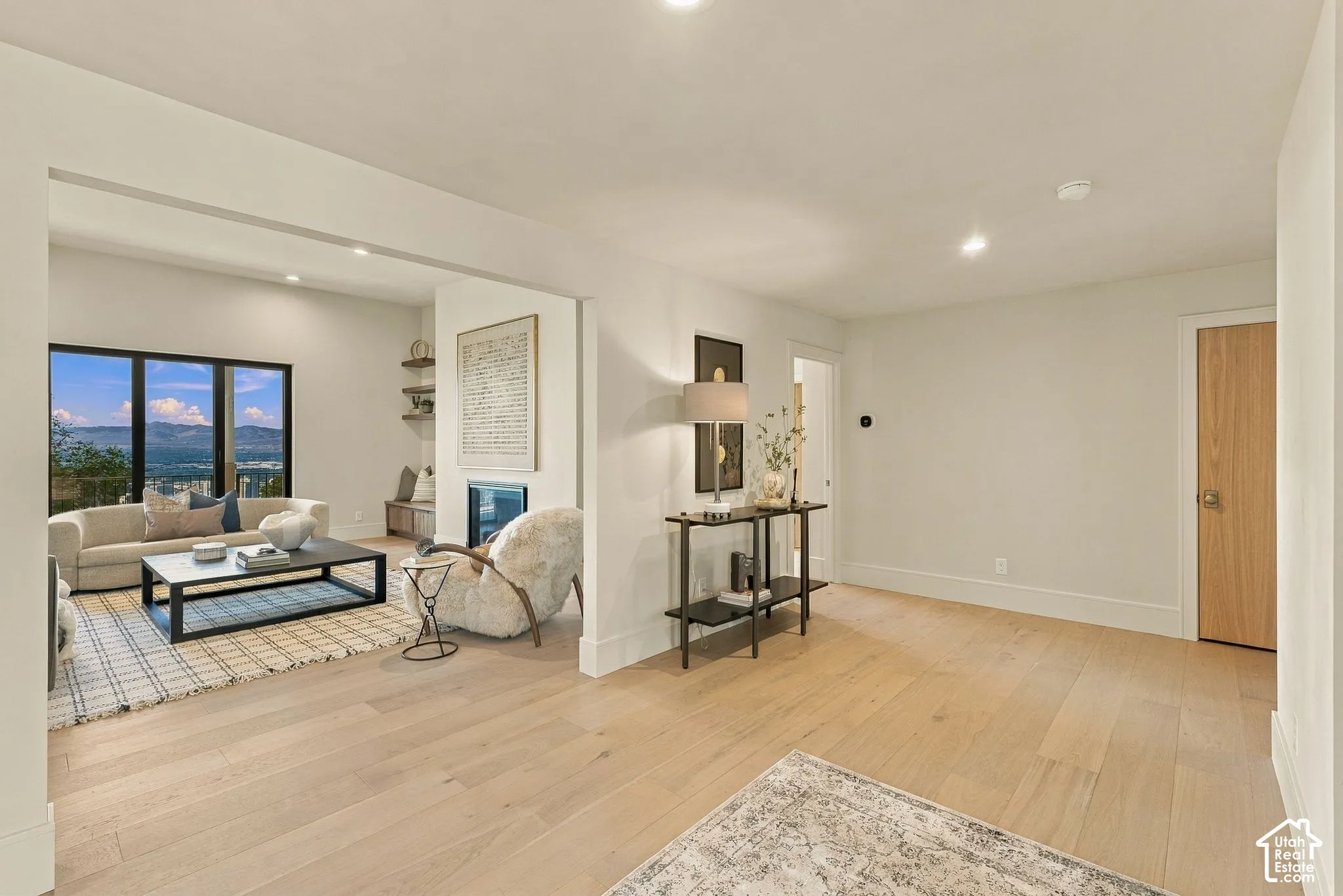 Light-toned wood-finish flooring, recessed lighting, built-in shelving, fireplace with a mantle, and large black-framed windows showcasing a mountain backdrop