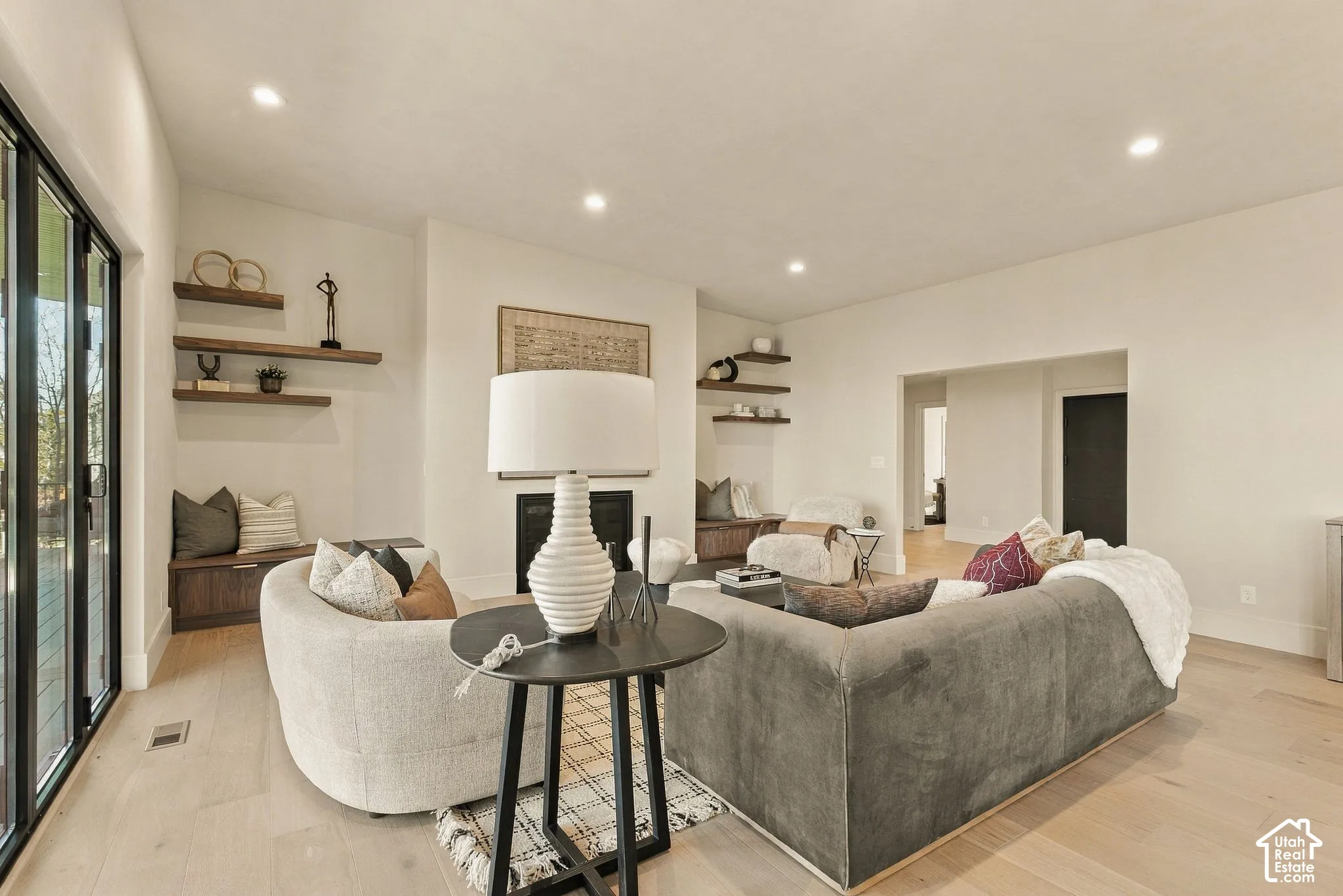 Living area featuring wood-finish flooring, recessed lighting, a fireplace, custom wall-mounted wood shelving, and multi-panel glass door systems