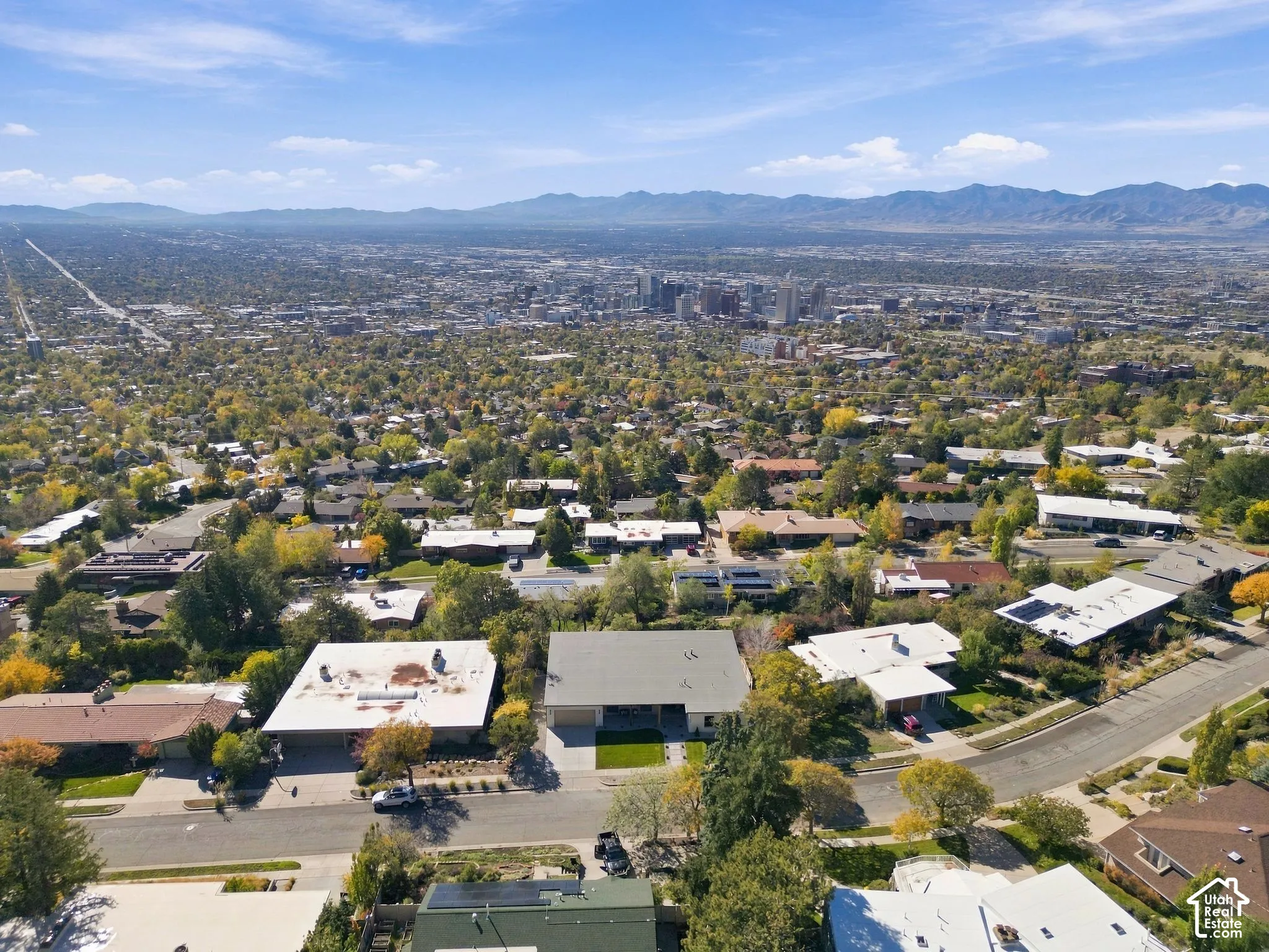 Aerial perspective featuring a single-story residence with a multi-car garage, manicured lawn, and extensive mountain and city skyline scenery