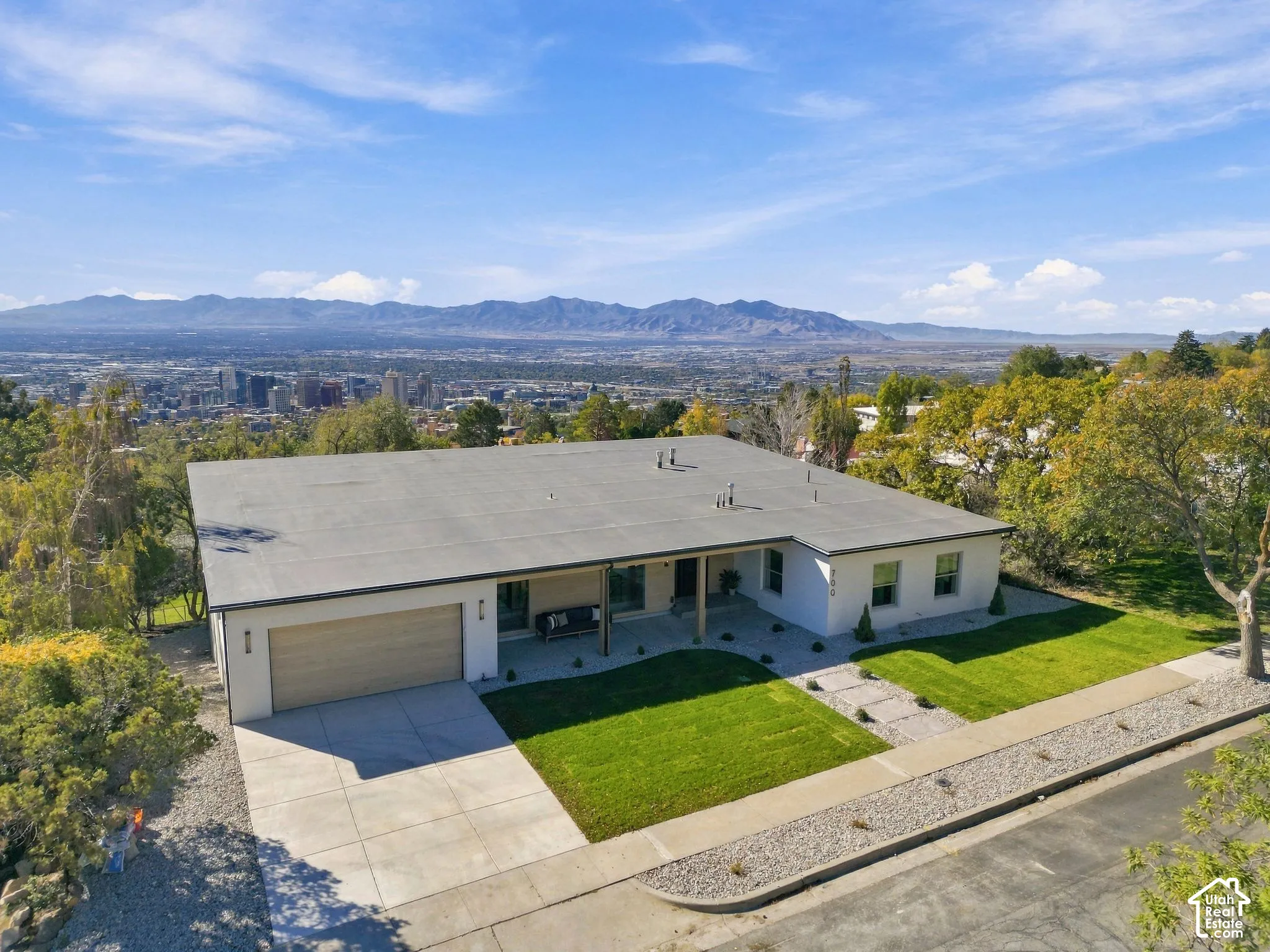 Mid-century modern residence featuring a smooth stucco exterior, a two-car garage, an expansive manicured lawn, and a wide concrete driveway, set against a mountainous skyline backdrop