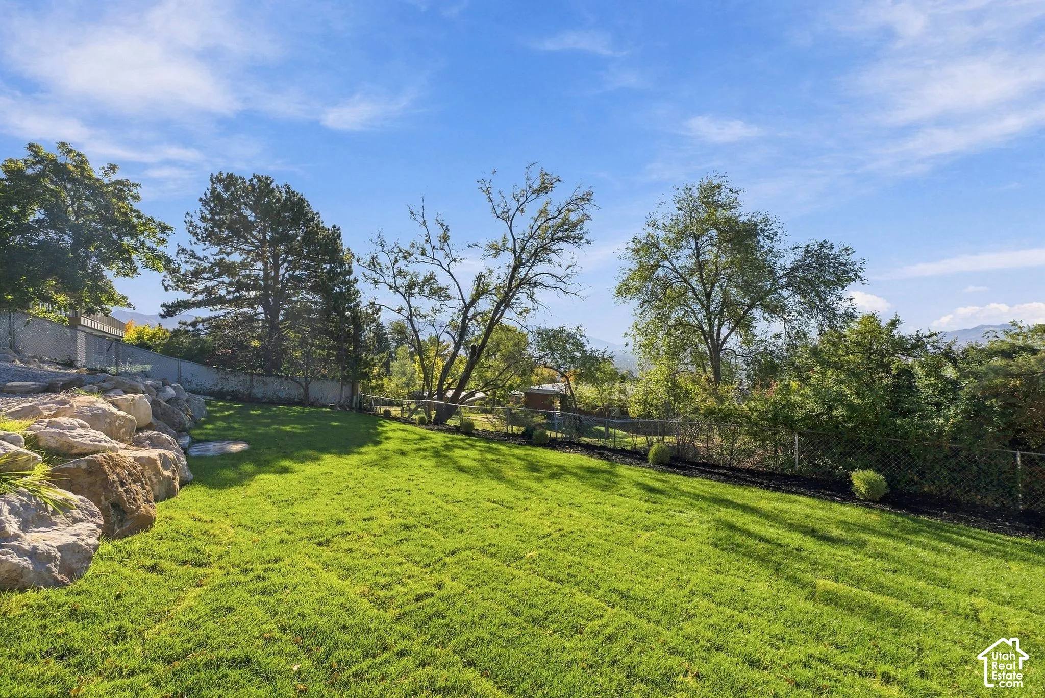 Expansive lawn area featuring natural stone rockery, mature trees, and perimeter fencing