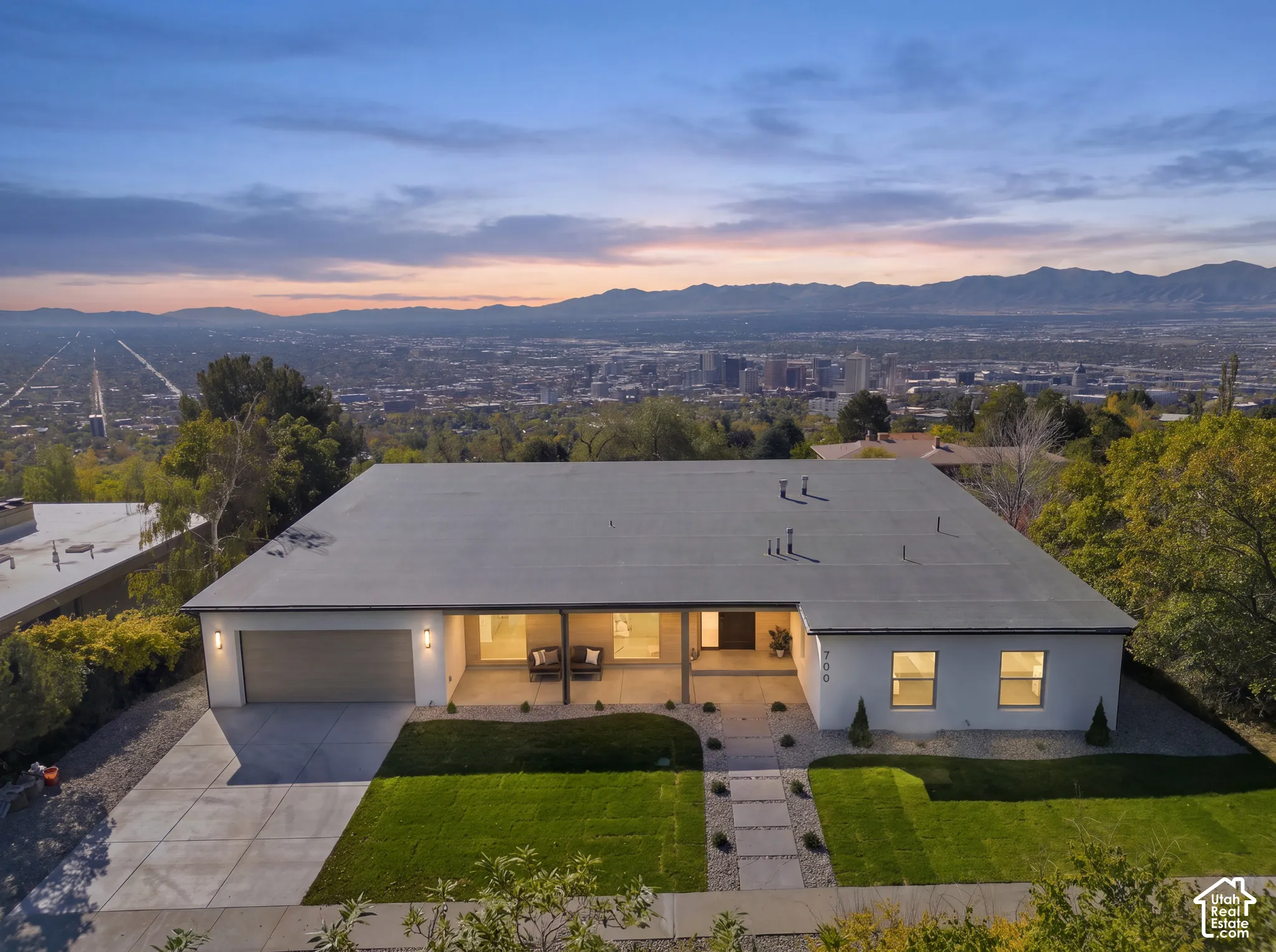Mid-century modern exterior featuring a smooth stucco facade, expansive attached garage, covered entryway, and concrete  walkway, with expansive mountain and valley horizon