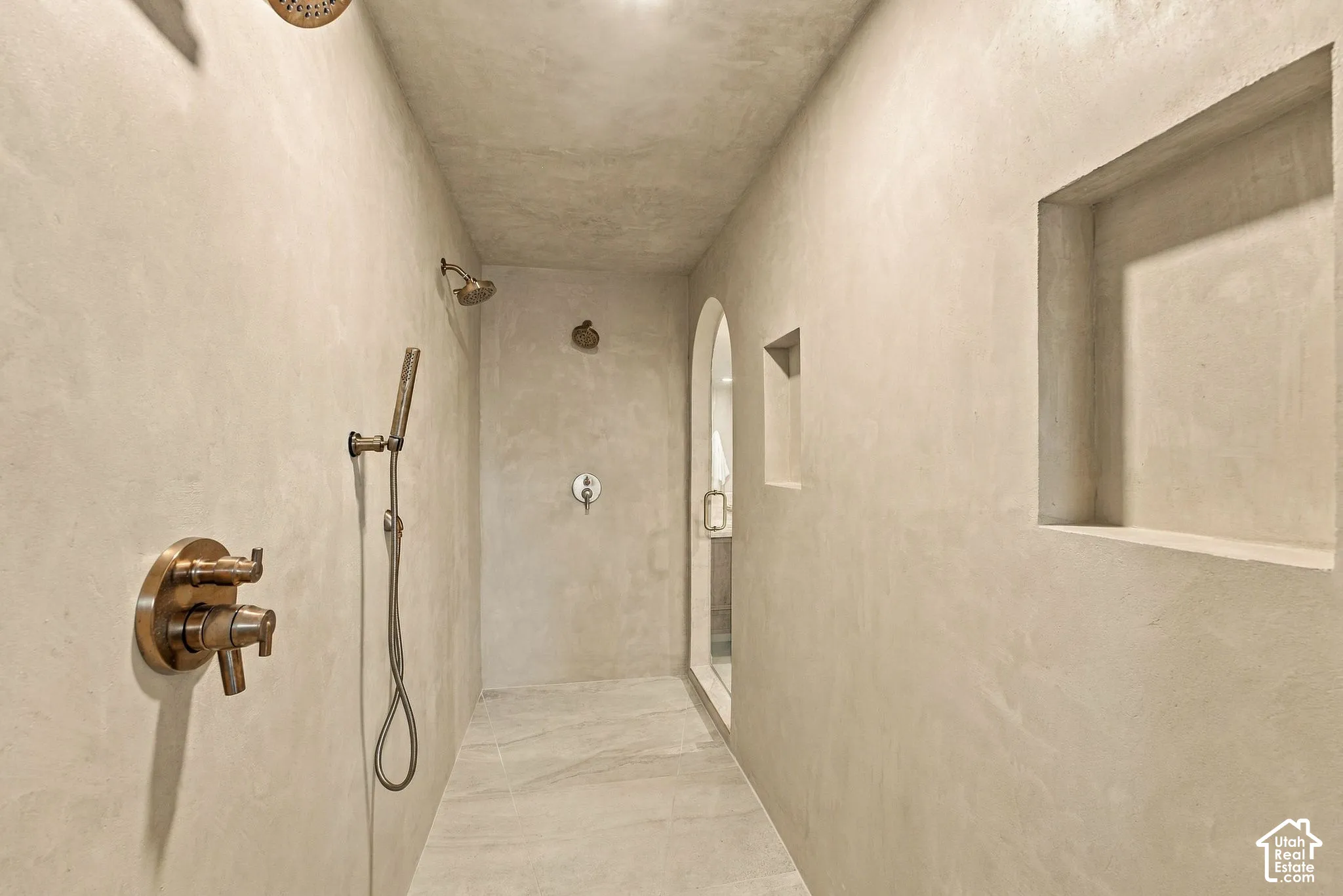 Walk-in shower featuring smooth-finish wall texture, dual-head fixtures with handheld sprayer, built-in wall niches, and large-format tile flooring
