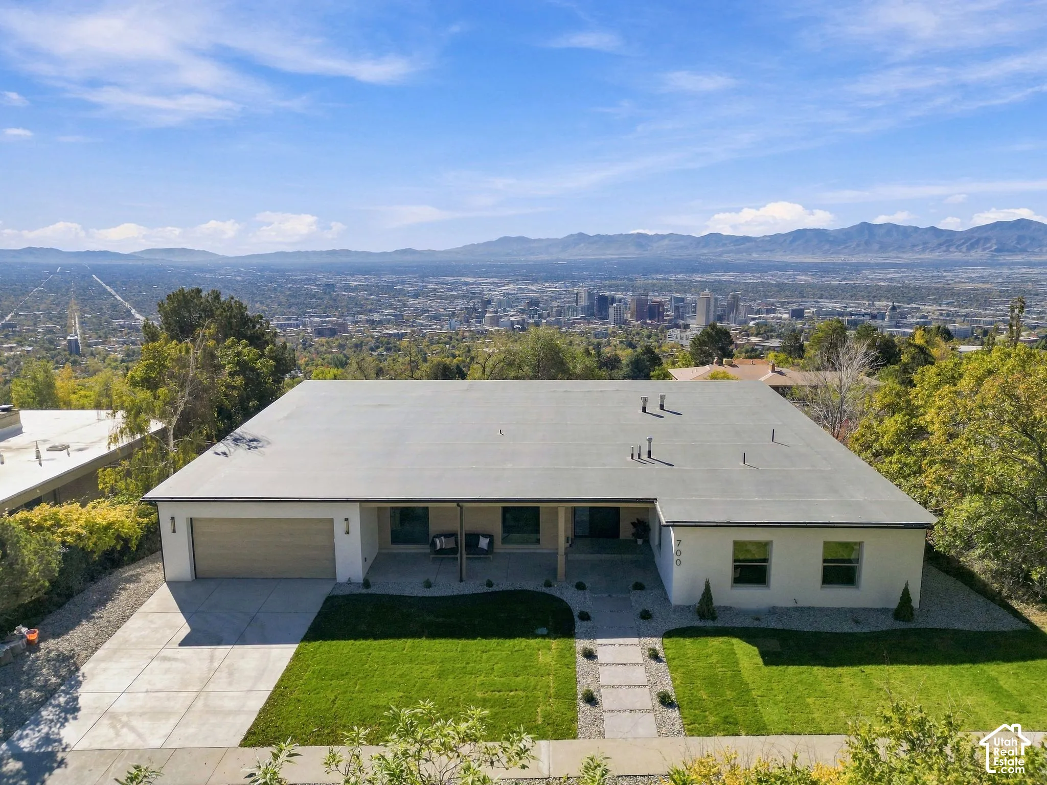Mid-century modern exterior featuring a flat roofline, attached two-car garage, low-maintenance gravel landscaping, manicured lawn, and sweeping mountain and city skyline panorama