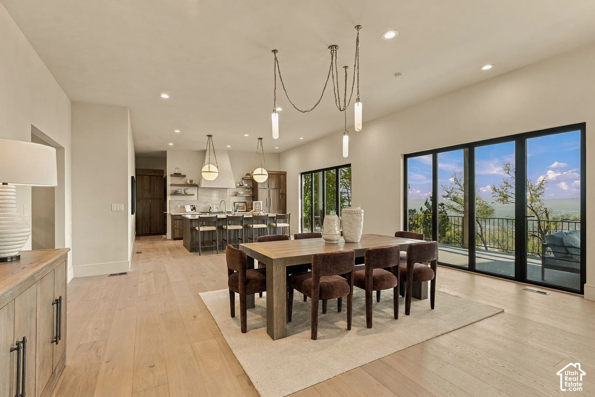 Open-concept interior featuring light wood-finish flooring, multi-paneled sliding glass doors, a kitchen island with stone countertops, and tiered multi-pendant lighting