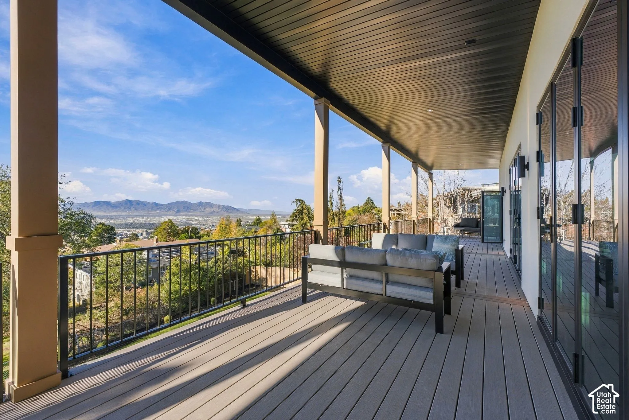 Covered deck featuring composite decking, black metal railing, structural support columns, and mountain scenery