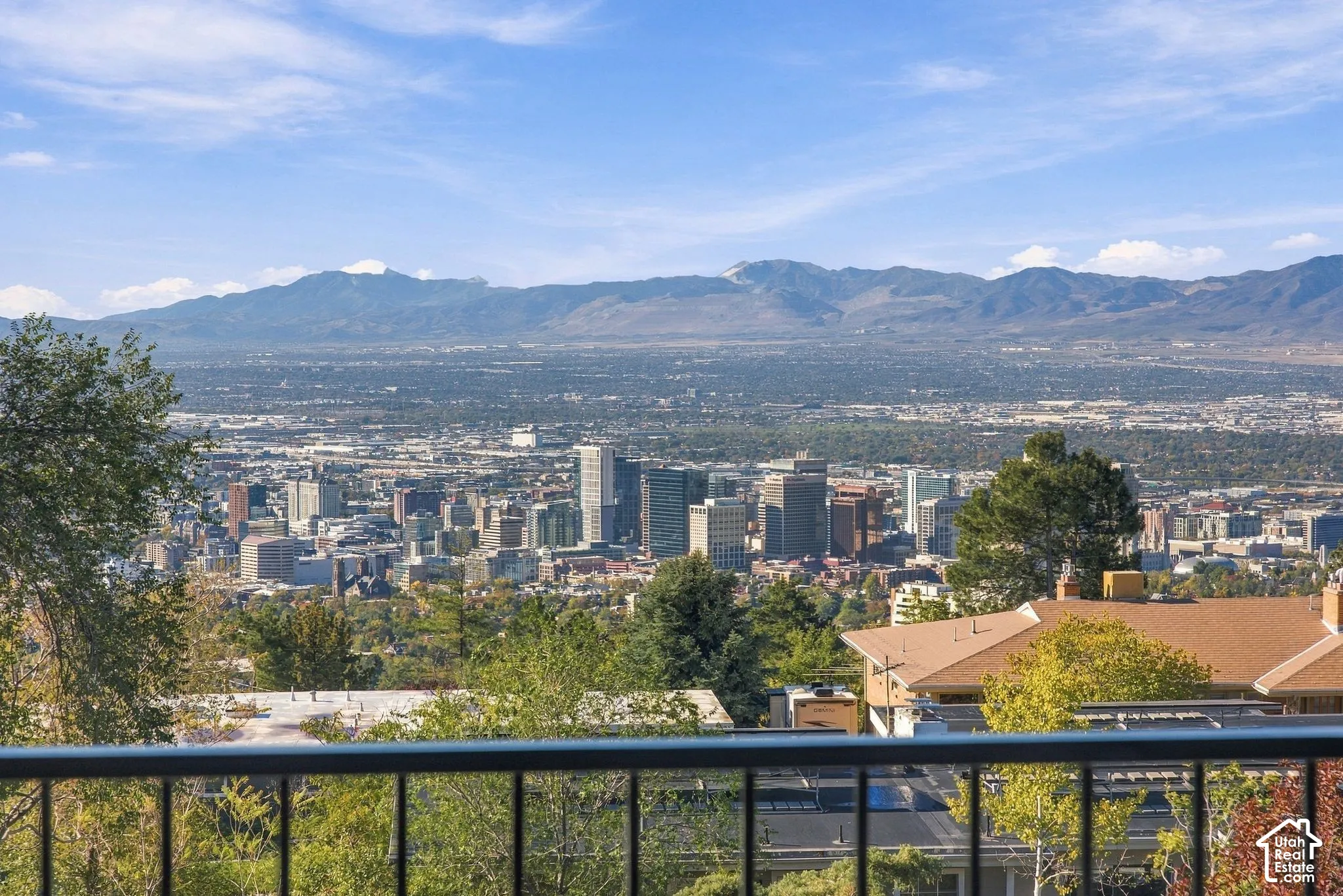 Elevated perspective featuring panoramic city skyline, expansive mountain range backdrop, and black metal balcony railing