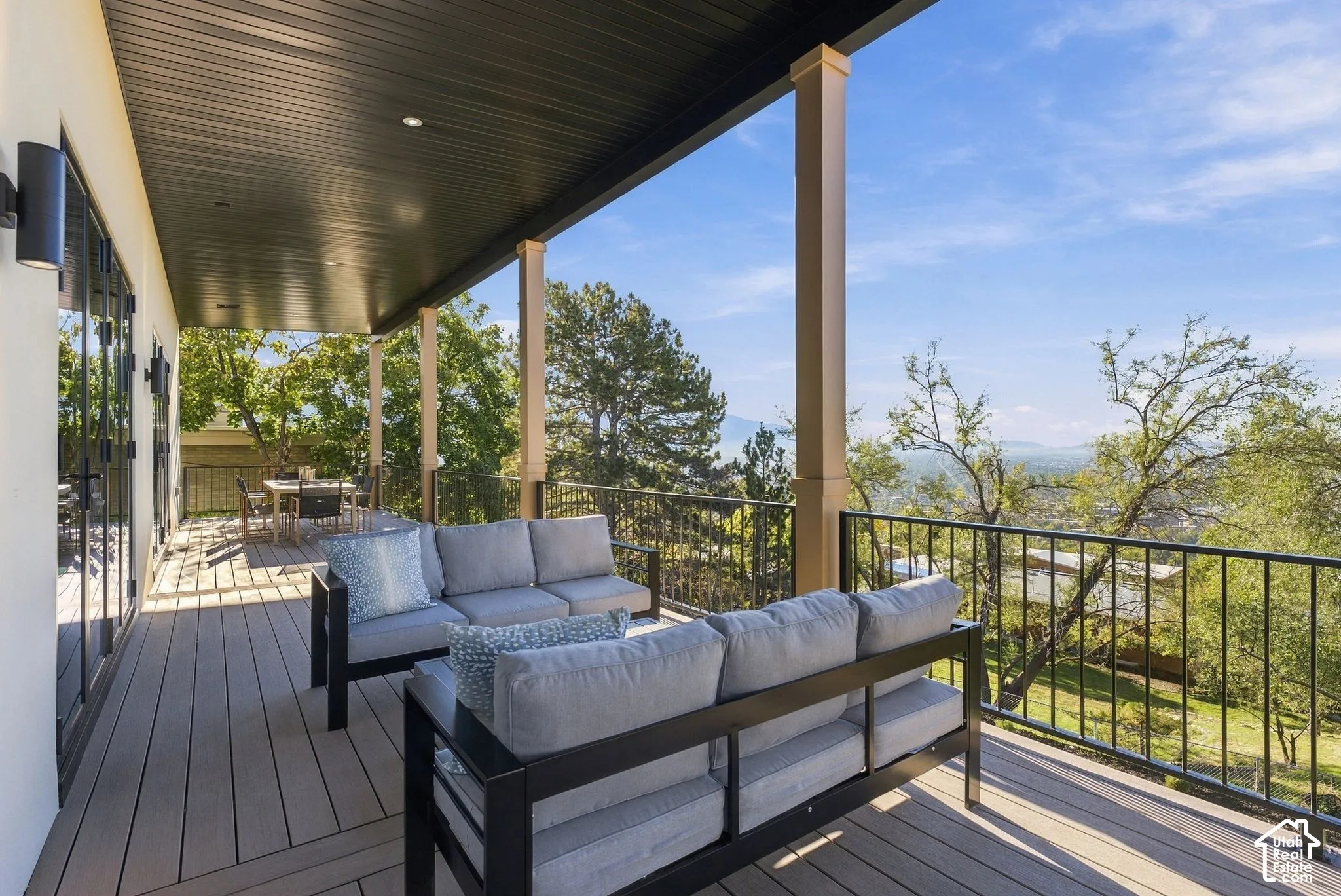 Covered deck featuring composite decking, recessed lighting, square support columns, and black metal railings with panoramic terrain scenery