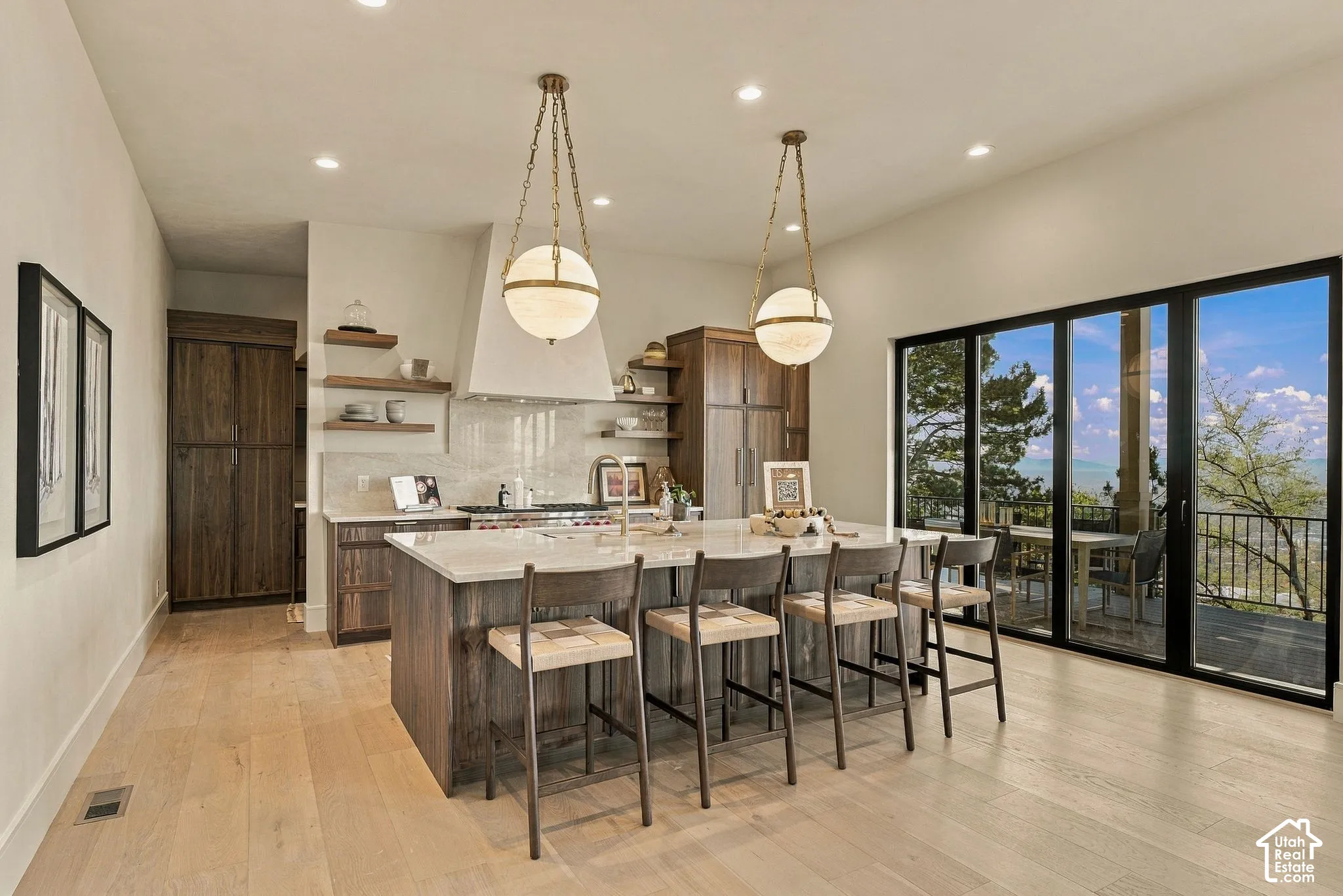 Kitchen featuring wood-finish flooring, a central island with stone-style countertops, custom cabinetry, dual globe pendant lighting, and multi-panel glass doors