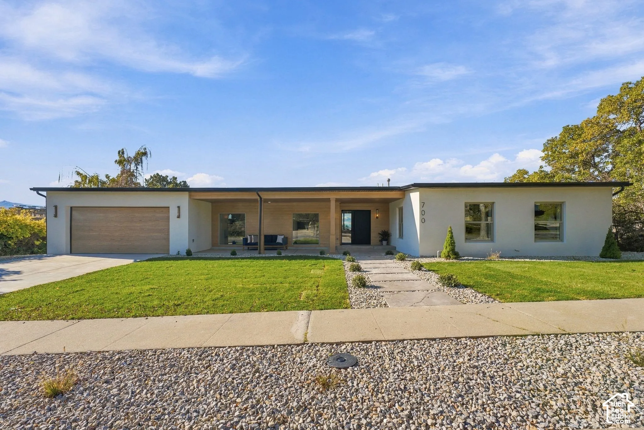 Mid-century modern exterior featuring a smooth-finish stucco facade, wood-finish garage door, covered porch with wood-clad ceiling, stone walkway, and manicured lawn