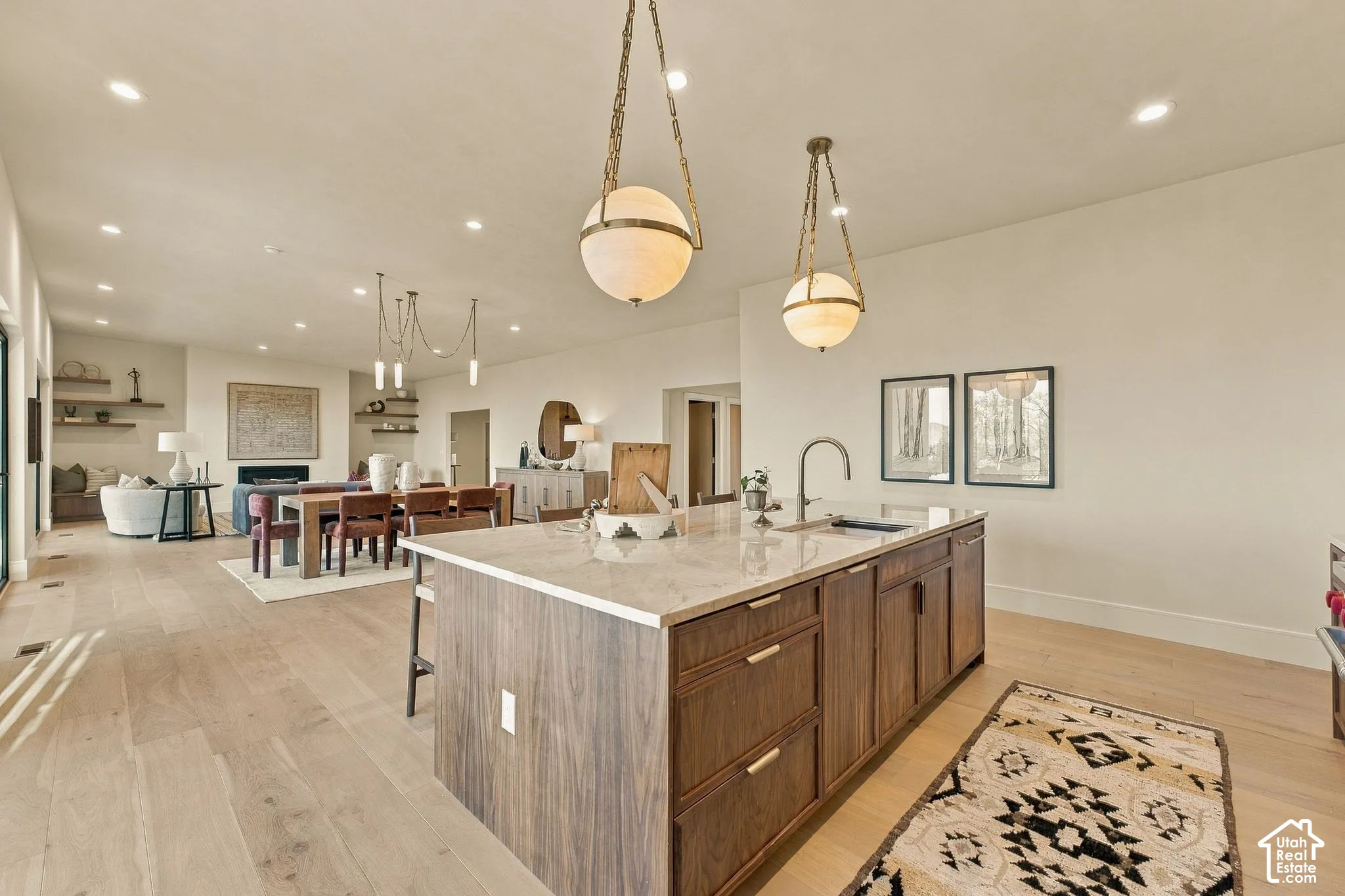 Kitchen island featuring wood-finish cabinetry, light-toned countertop, and undermount sink, complemented by dual spherical pendant lighting and wood-finish flooring throughout