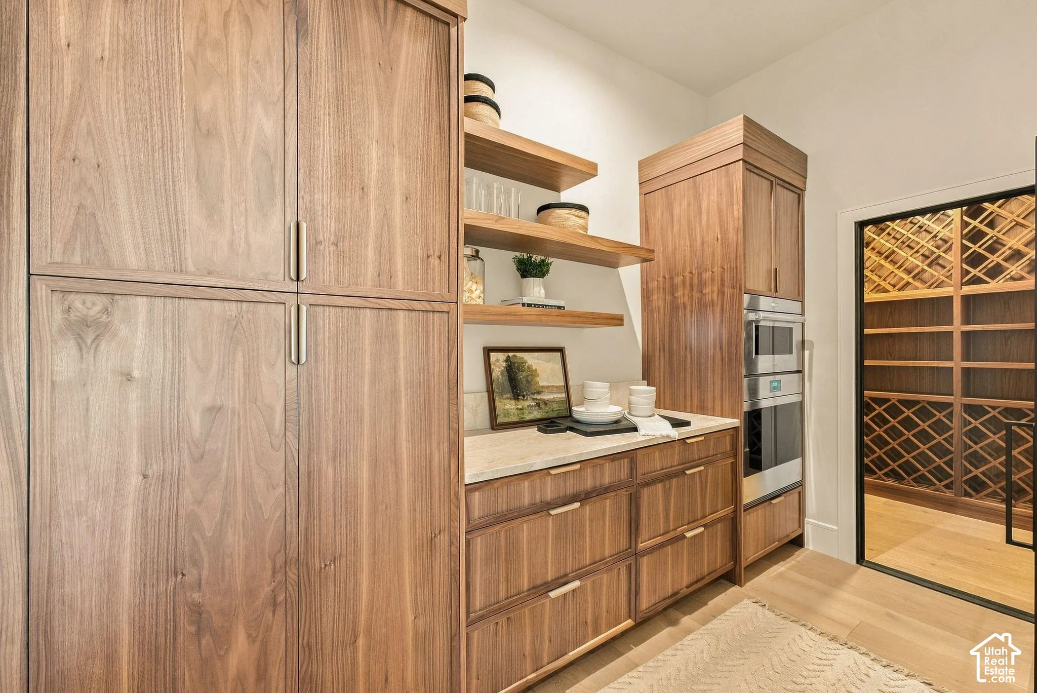 Custom wood-finish cabinetry, built-in dual stainless steel ovens, stone countertop, floating wood-finish shelving, and dedicated climate-controlled storage with wine racking