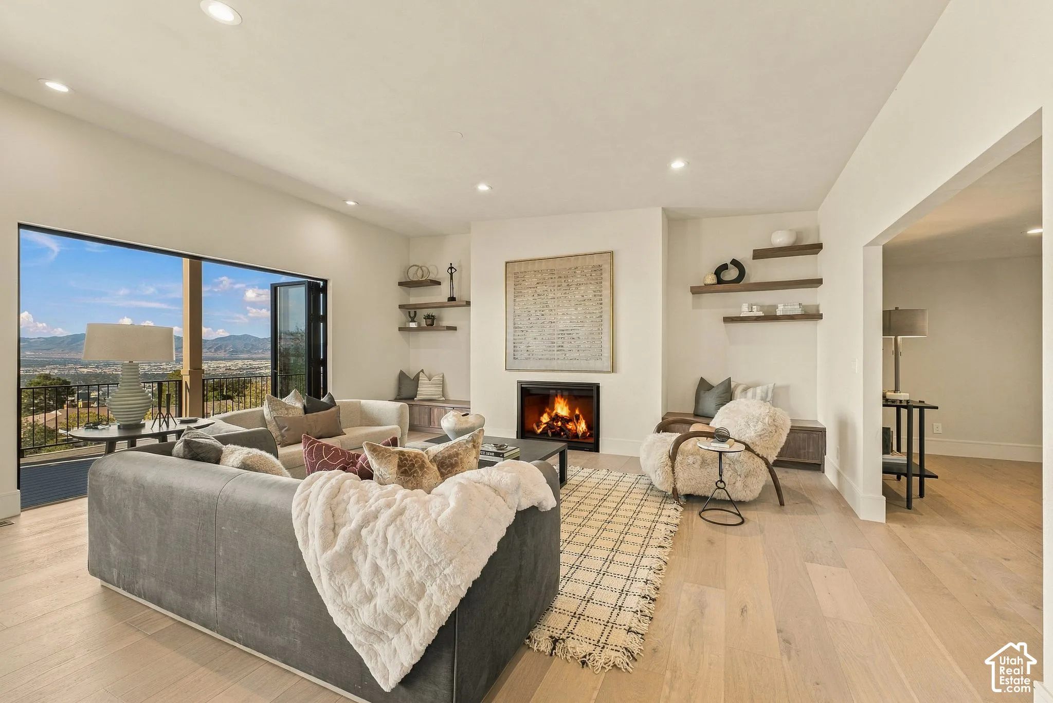 Living area featuring wood-finish flooring, a recessed fireplace, built-in lower cabinetry with floating shelves, and a multi-panel door system opening to an exterior terrace with mountain scenery